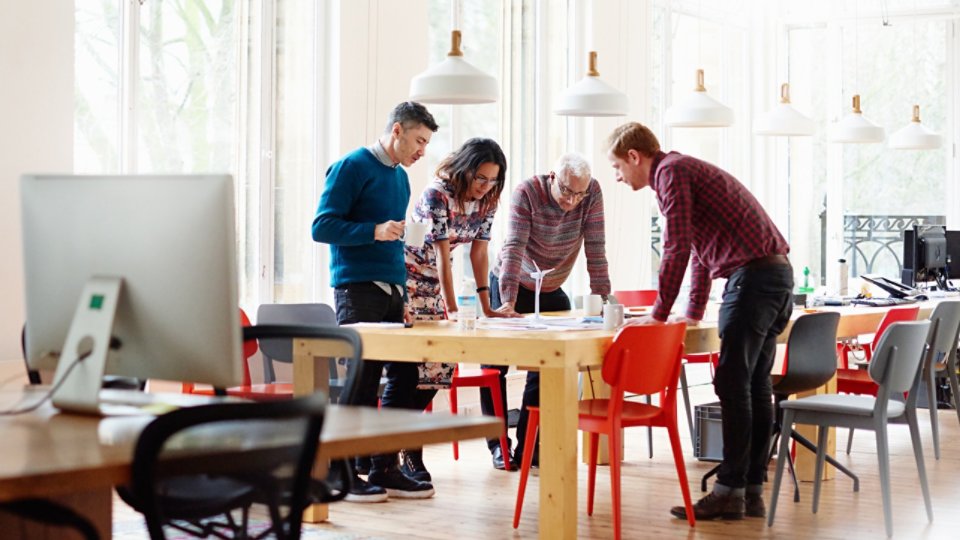 A group of four colleagues standing in an elegant modern office discussing a green energy project