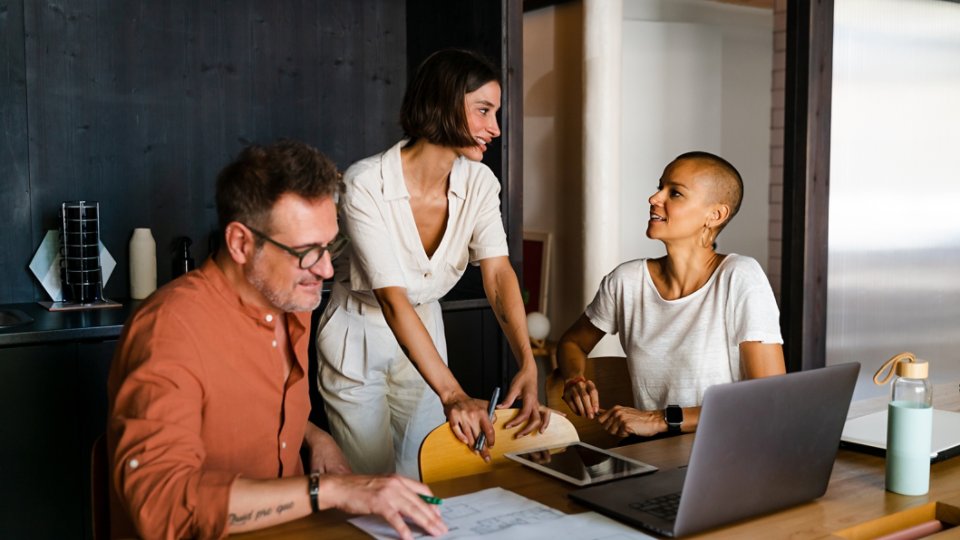 Teamwork talking at business meeting sharing ideas while discussing project. People sitting around the table with computers and documents.