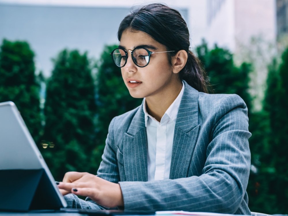 Spanish business woman in classic glasses for provide eyes protection typing information text while working remotely with online project, formally dressed female trader in spectacles searching data