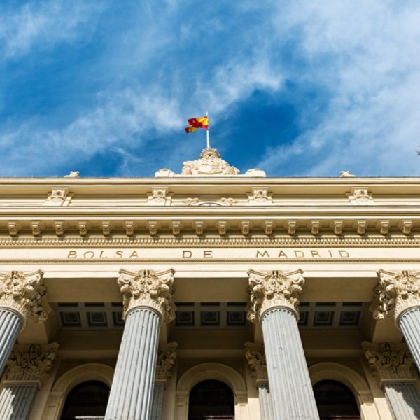 Low-angle view of the columns and neoclassical facade of the Bolsa de Madrid (Madrid's Stock Exchange) against a cloudy blue sky.