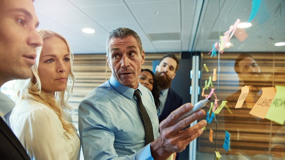 Businessman in a meeting with colleagues grouped around ideas on sticky memos looking aside with an attentive expression as he listens to a team member