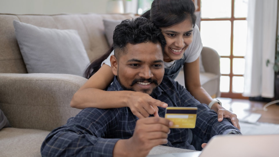 Happy indian couple with bank card and laptop at home, Young caucasian couple smiling happy using laptop and credit card