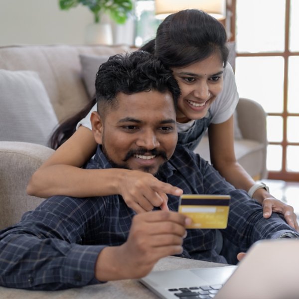 Happy indian couple with bank card and laptop at home, Young caucasian couple smiling happy using laptop and credit card.