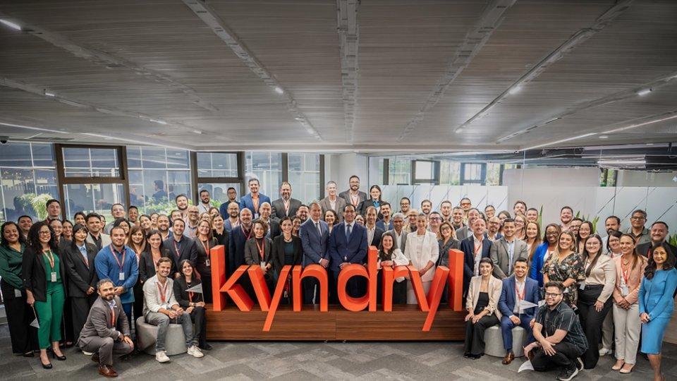 Kyndryl employees standing around the a 3D sculpture of the logo