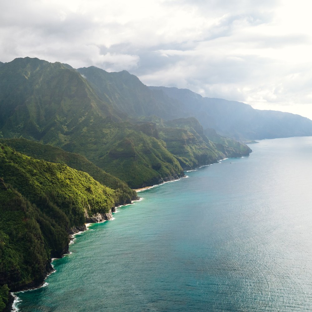 Aerial view of a coastal travel destination in Hawaii, a rugged coastline with green cliffs and tranquil waters in Kauai. View of the beautiful coastline in Ne Pali State Park.