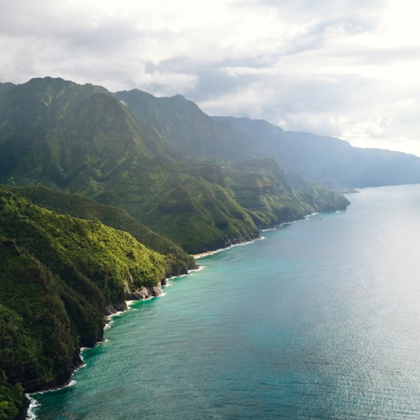Aerial view of a coastal travel destination in Hawaii, a rugged coastline with green cliffs and tranquil waters in Kauai. View of the beautiful coastline in Ne Pali State Park.