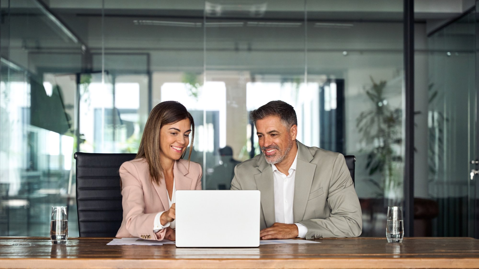 Professional business executive managers office team working using laptop computer sitting at table. Two middle aged colleagues company board discussing digital strategy at corporate meeting.