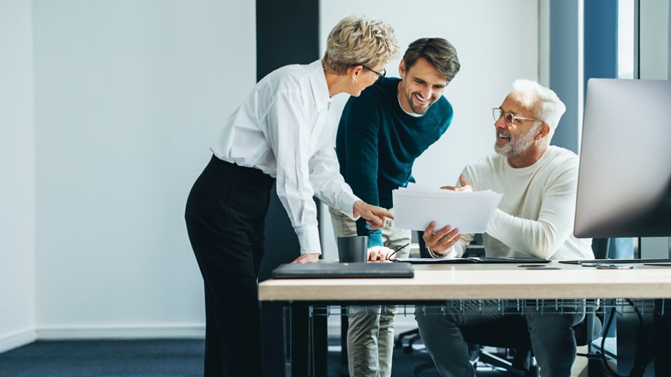 Three business people huddling and discussing a document in an office. Group of business professionals contributing their ideas and expertise as they collaborate on a project for their startup.