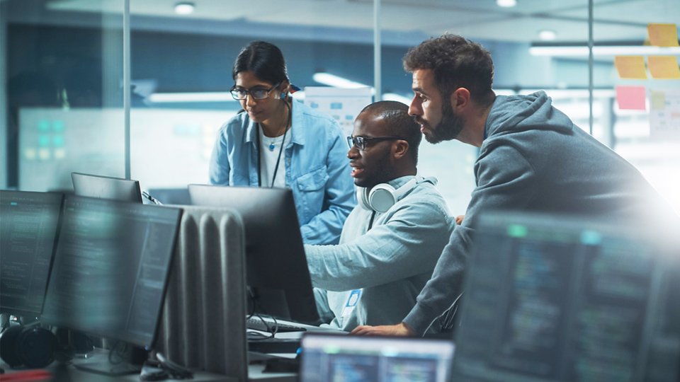 Two men and a woman in discussion around a workstation