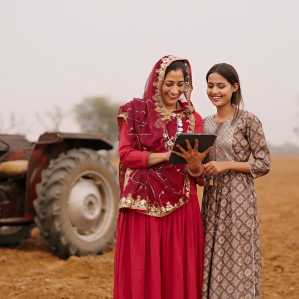Indian asian villager farmer young adult woman lady wear red saree smiling outdoor hold tab device browse website data happy teen age girl teach mom talking enjoy day time outside desi life