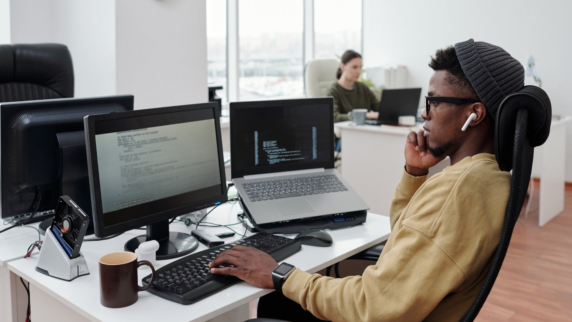 Side view of young serious lack man concentrating on decoding data while sitting in front of computer monitor by workplace in office