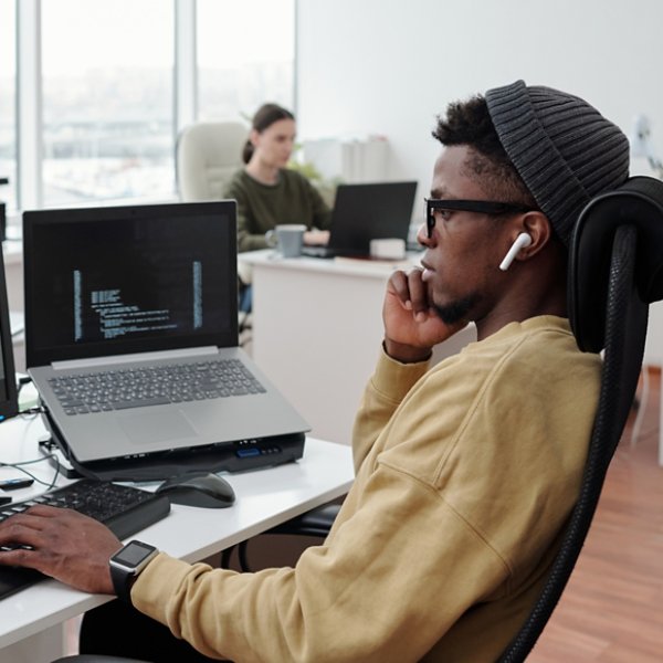 Side view of young serious lack man concentrating on decoding data while sitting in front of computer monitor by workplace in office