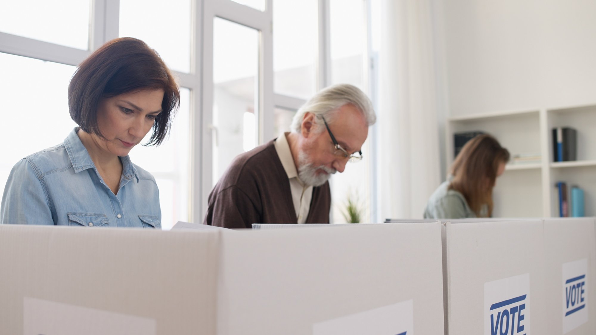 Concentrated men and women are reading information on election ballots before casting their votes