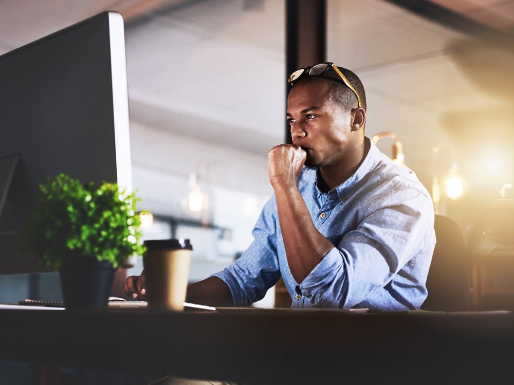 Thinking, computer and business black man in office for website, research and reading news at night. Startup, developer and worker online for software update, networking and working on web design.
