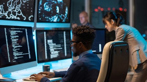 Young it-engineer decoding data while sitting in front of computer monitors and looking at screen of one of them