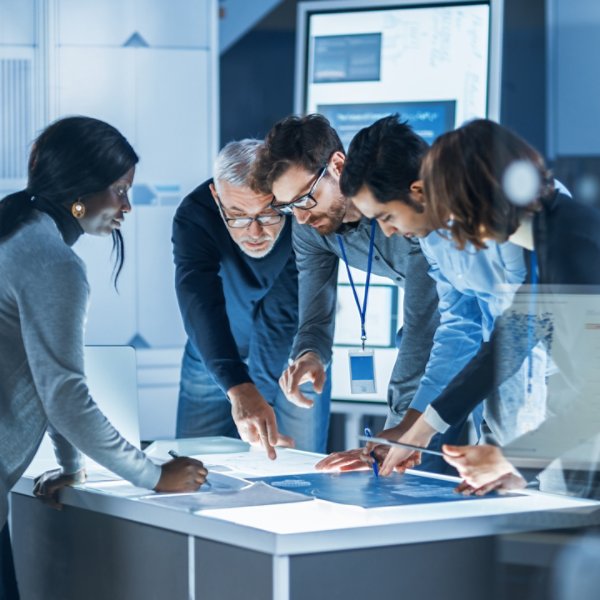 Engineers Meeting in Technology Research Laboratory: Engineers, Scientists and Developers Gathered Around Illuminated Conference Table, Talking and Finding Solution, Inspecting and Analysing Industrial Engine Design.