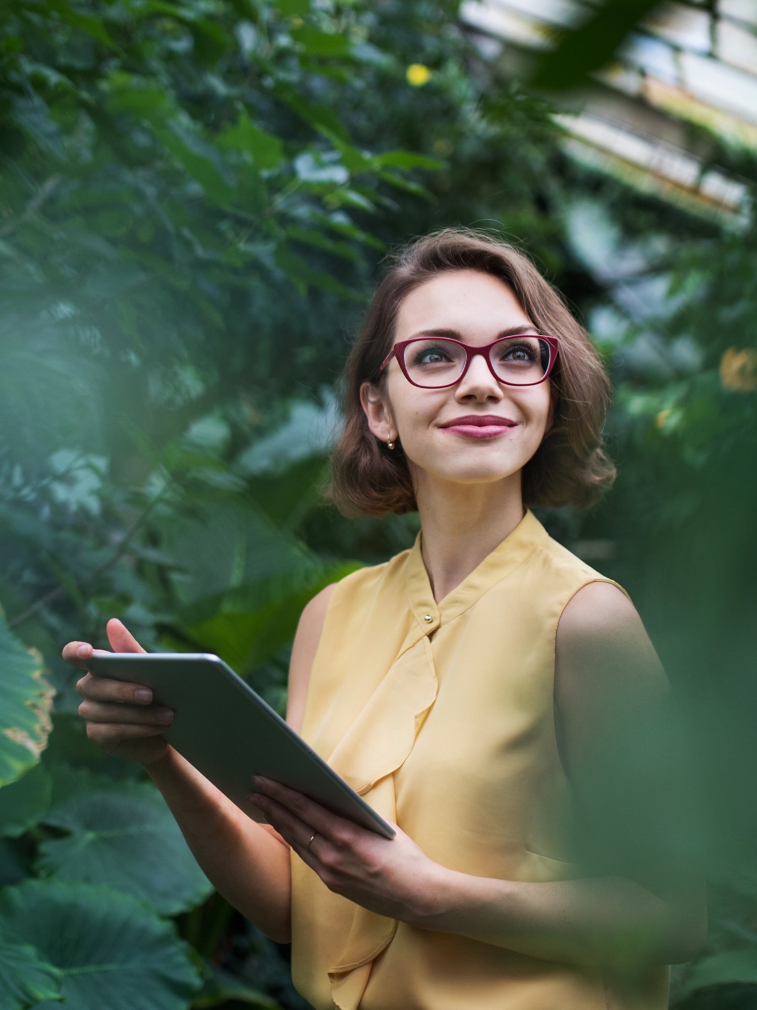 Young woman with tablet standing in greenhouse in botanical garden. Copy space.