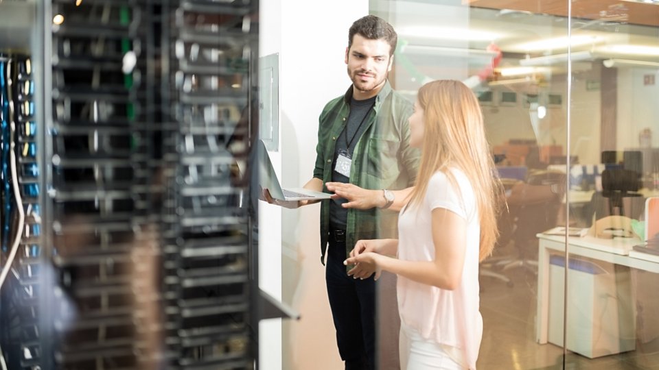Two business people standing in server room with laptop and discussing