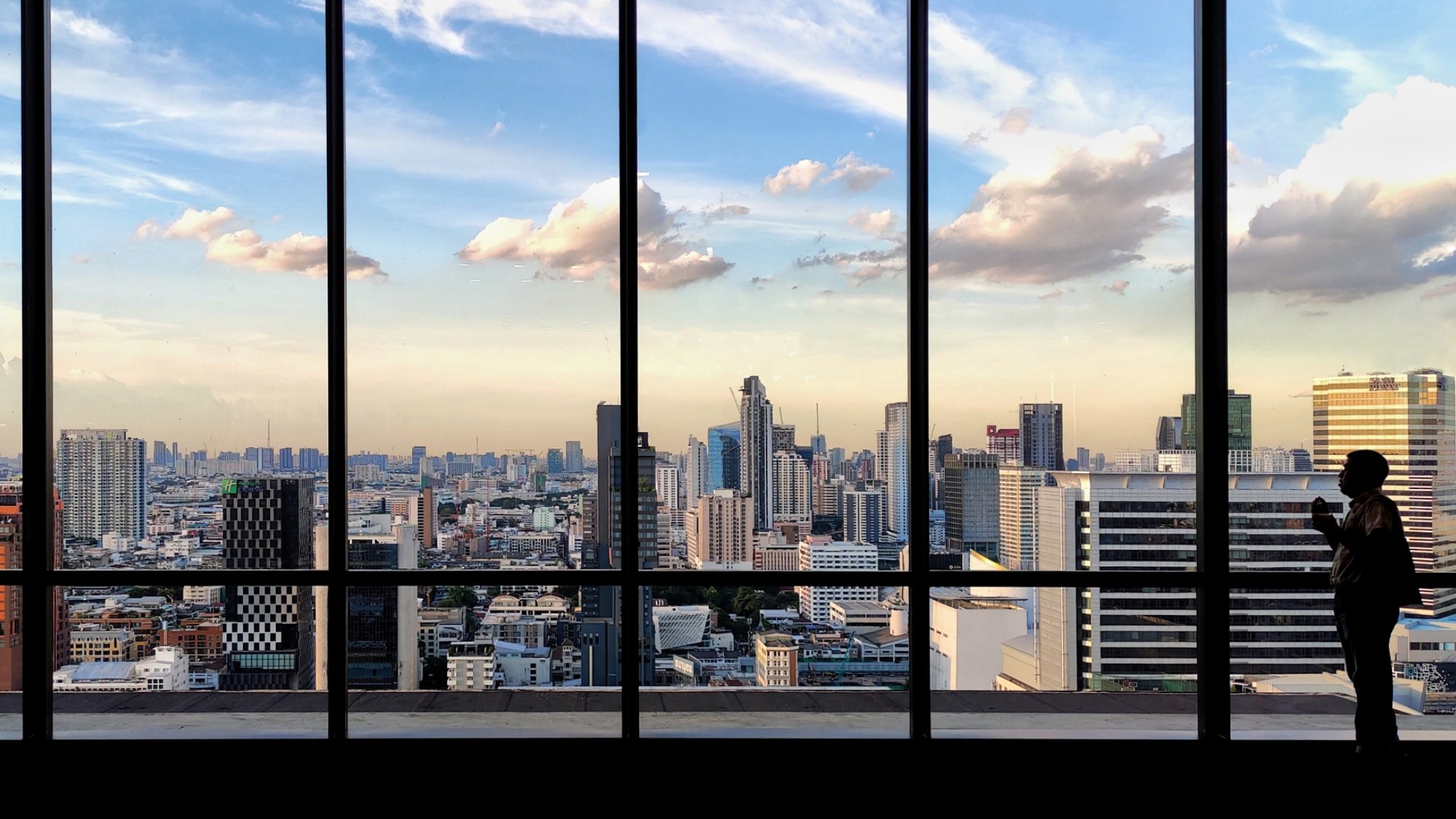 silhouette outline of women tourist taking pictures of city skyline from an observatory. sunset at modern urban business district. steel frame rose windows architectural element design.