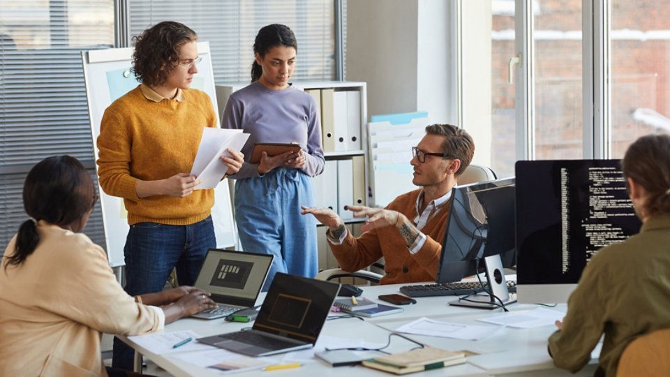 Portrait of diverse software development team collaborating on project in modern office, focus on lead engineer instructing colleagues, copy space