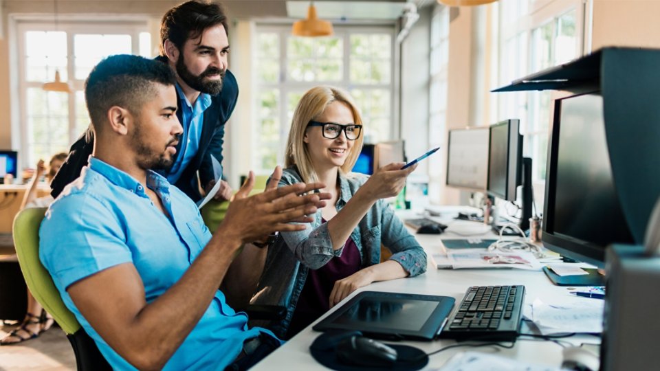 Three employees in discussion and pointing to whats on the workstation screen