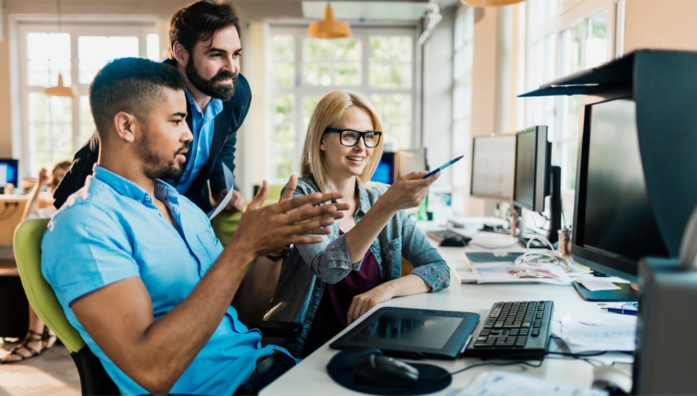 Three employees in discussion and pointing to whats on the workstation screen