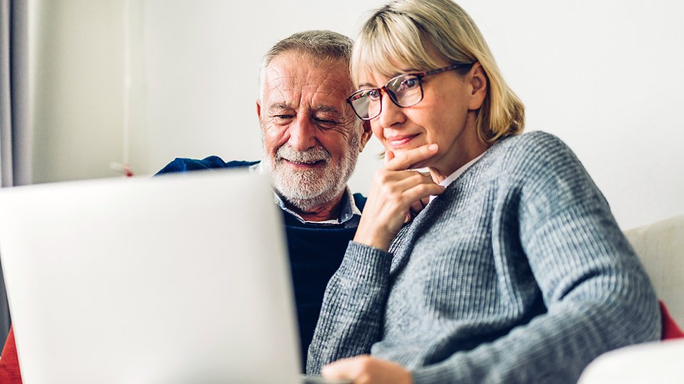 Senior couple family having good time using laptop computer together.Happy elderly husband and wife checking social media and reading news or shopping online while sitting on sofa at home