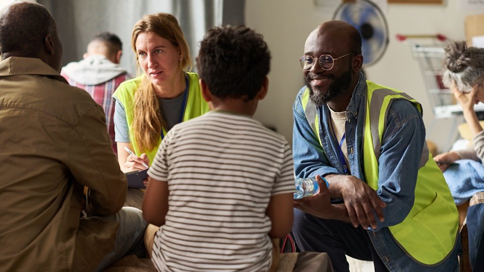 African American man, Caucasian woman volunteers meeting family, listening and taking notes at relief center. Ideal for community support, social services, nonprofit outreach marketing