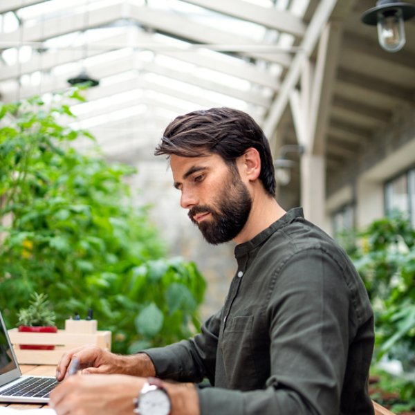 Portrait of young man with laptop sitting indoors in green office, working.