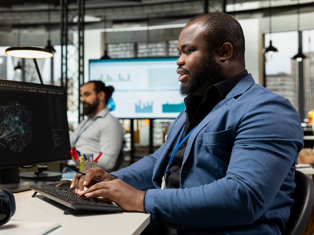 Black IT technician employs neural networks and pattern recognition for a software to drive transformation and improve decision making, with big data deep learning systems for optimization.