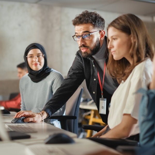 Lecturer Helps Scholar with Project, Advising on Their Work. Teacher Giving Lesson to Diverse Multiethnic Group of Female and Male Students in College Room, Teaching New Academic Skills on a Computer.