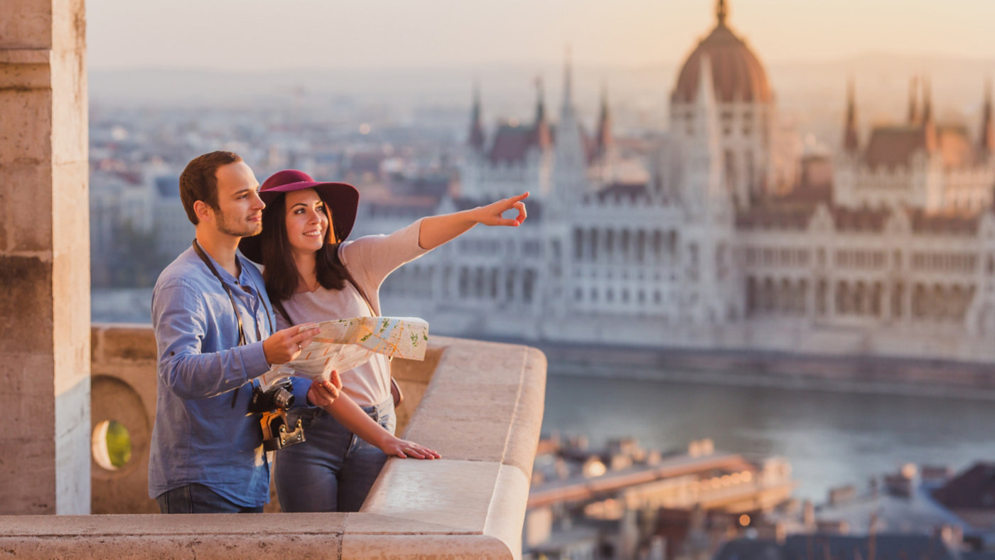 Young couple searching right direction on map from the point from Fisherman Bastion in Budapest with Hungarian Parliament building on background during sunrise