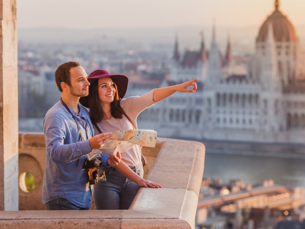 Young couple searching right direction on map from the point from Fisherman Bastion in Budapest with Hungarian Parliament building on background during sunrise
