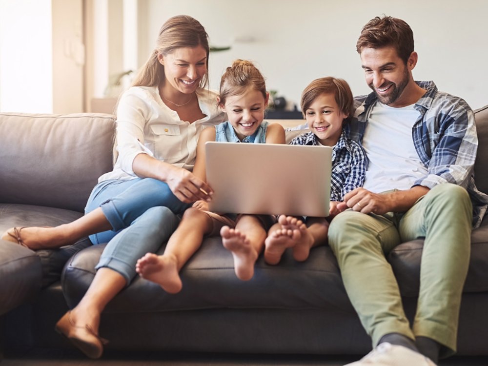 Family, laptop and kids with parents on a living room sofa with education game online. Mom, dad and young children together with bonding, parent care and love in a house watching a video on computer.