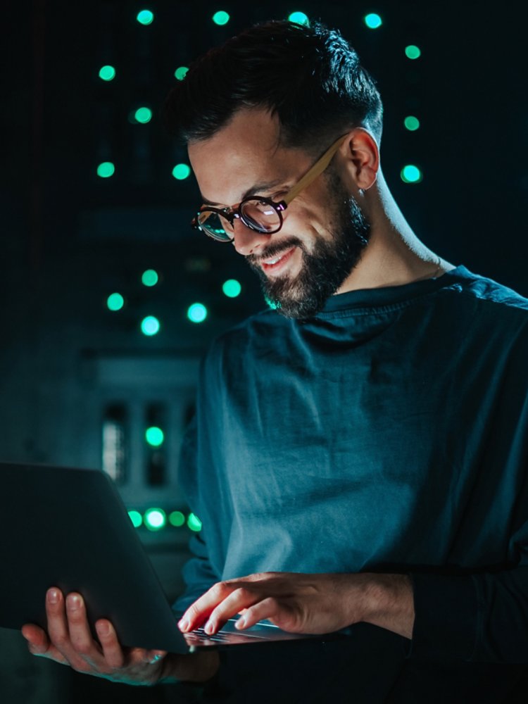 Young smiling it professional using laptop in server room, performing network engineering and cybersecurity tasks for data management