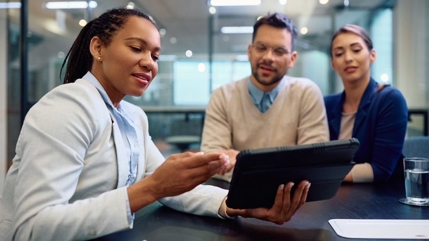 Black insurance agent and her clients using digital tablet during meeting.