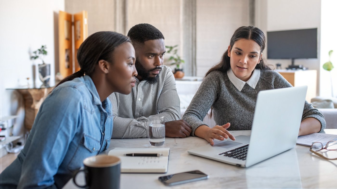 Financial planner going over savings plans on a laptop with a young African American couple at a table in their living room at home