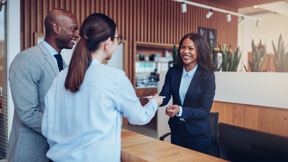 Two guests giving their reservation details to a smiling concierge while checking in together at the reception counter of a hotel