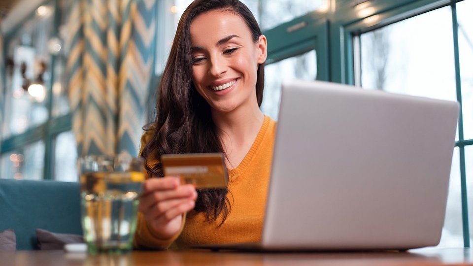 Advanced payment. Optimistic energetic calm woman using credit card while gazing down and laptop standing on table