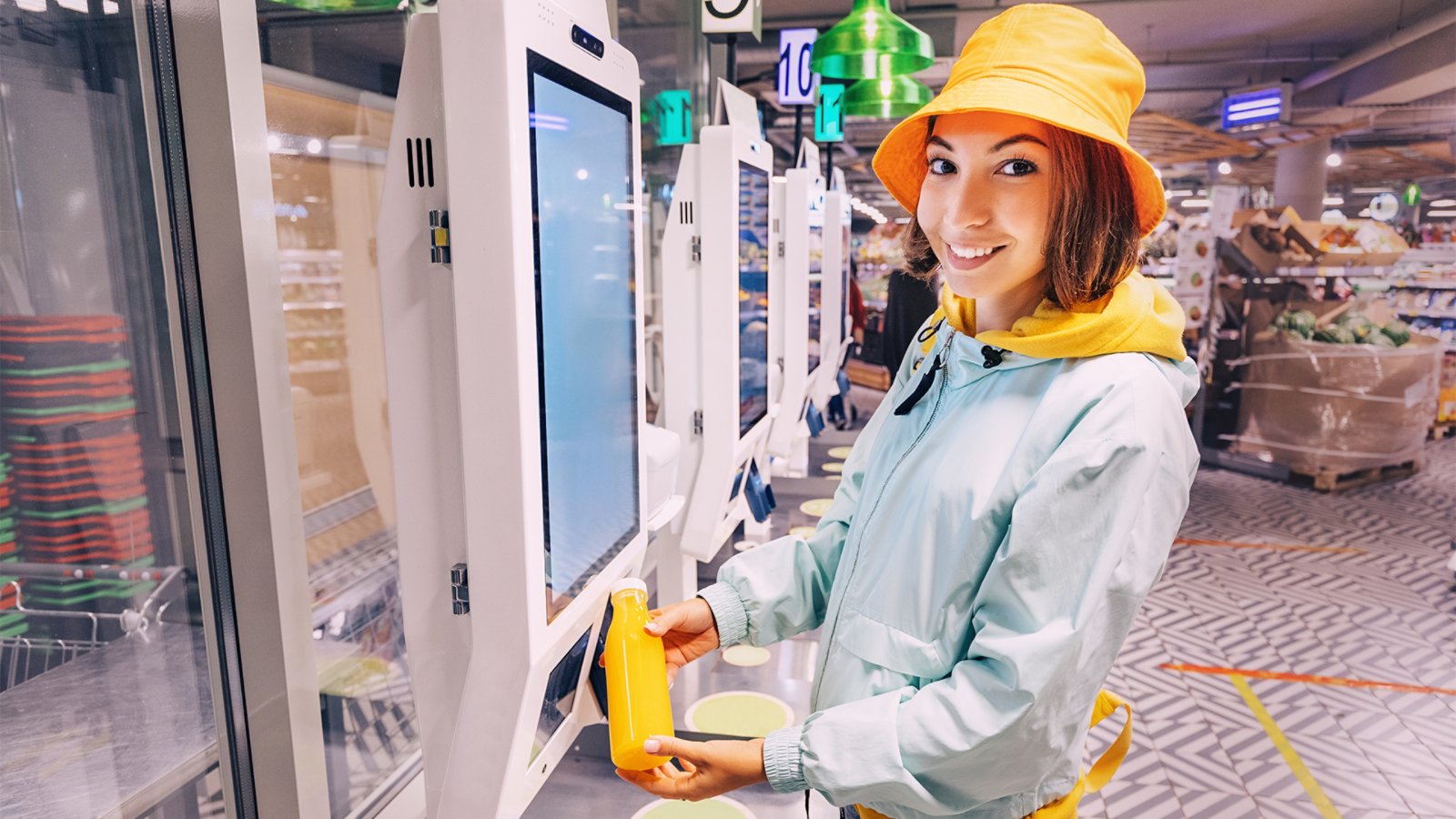 Happy young customer woman buys and pays for a bottle of orange juice at the checkout of a self-service vending machine in a modern supermarket, to avoid waiting in line