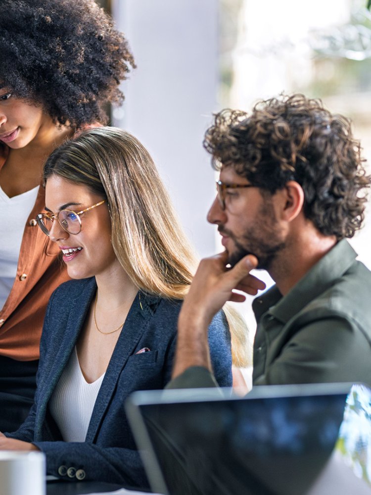 Blond businesswoman using laptop and talking with colleagues in office