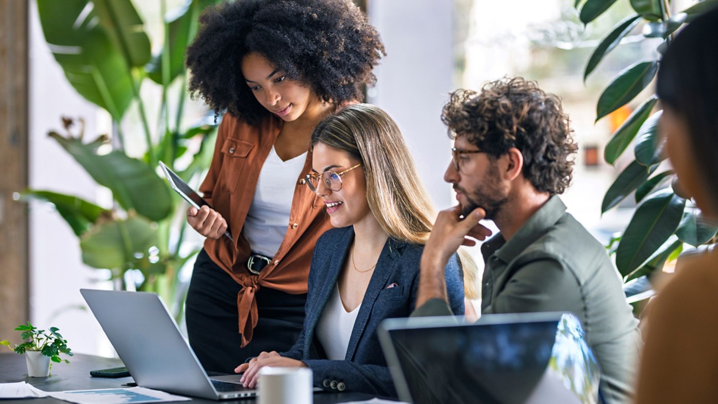 Blond businesswoman using laptop and talking with colleagues in office