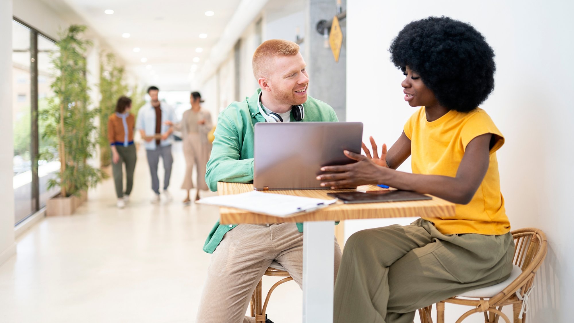 Two office workers are discussing a project, using a laptop and a tablet in a modern office environment