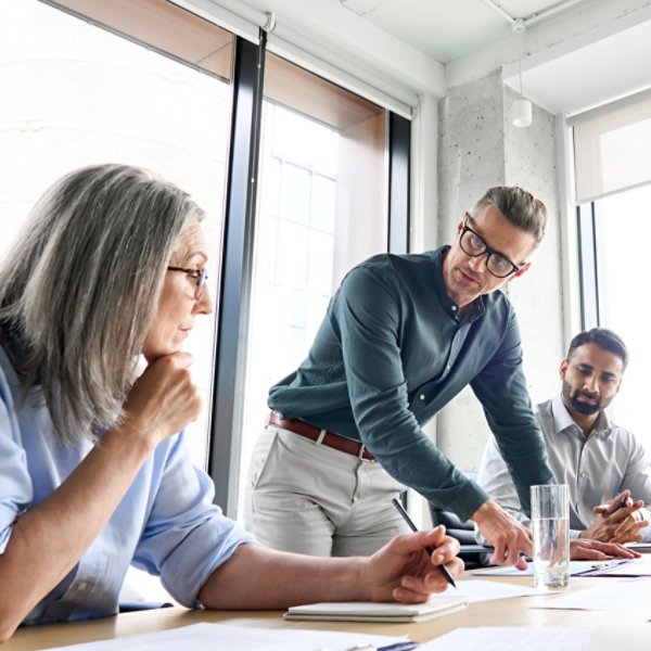 Male mature caucasian ceo businessman leader with diverse coworkers team, executive managers group at meeting. Multicultural professional businesspeople working together on research plan in boardroom.