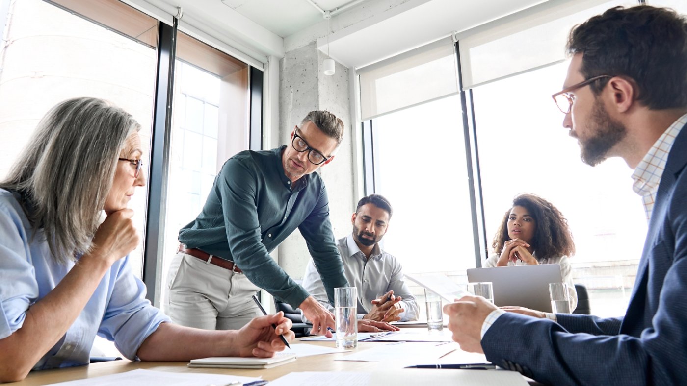 Male mature caucasian ceo businessman leader with diverse coworkers team, executive managers group at meeting. Multicultural professional businesspeople working together on research plan in boardroom.