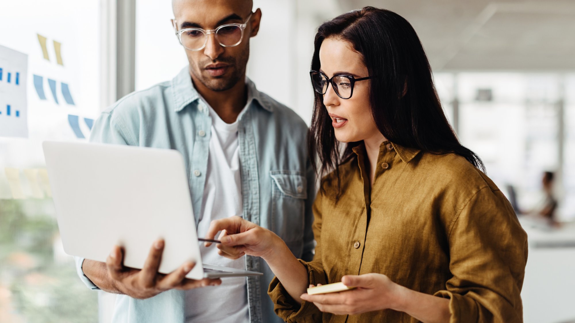 Business people standing in an office and using a laptop together. Two young professionals having a discussion in a workplace.