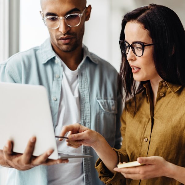 Business people standing in an office and using a laptop together. Two young professionals having a discussion in a workplace.