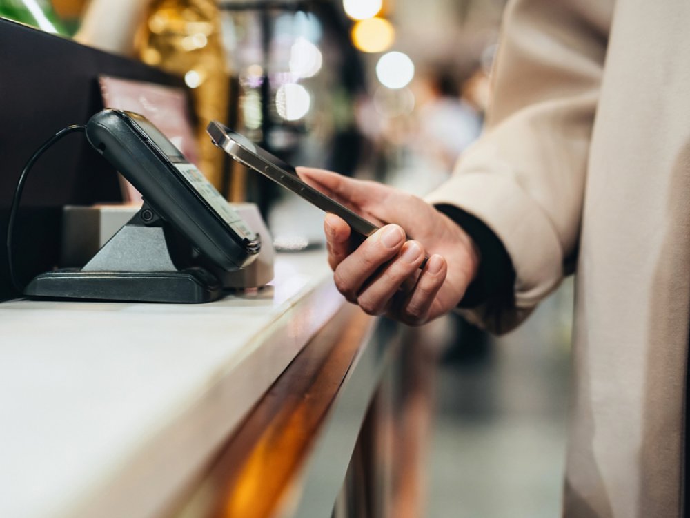 Close-up shot of woman's hand making credit card mobile payment with her smartphone in a store, scan and pay a bill on a card machine making a quick and easy contactless payment at checkout counter. NFC financial technology, tap and go concept