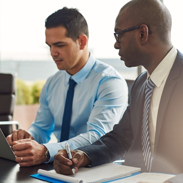 Two experienced business executives in a meeting seated at a table discussing paperwork and information on a laptop computer, one Hispanic, one African American