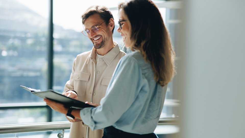 Business professionals going though a report document together in an office. Two business colleagues smiling as they read on the growth and success of their company.